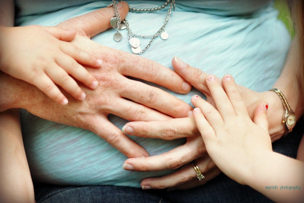 Family hands on pregnant belly by Katie M Reid