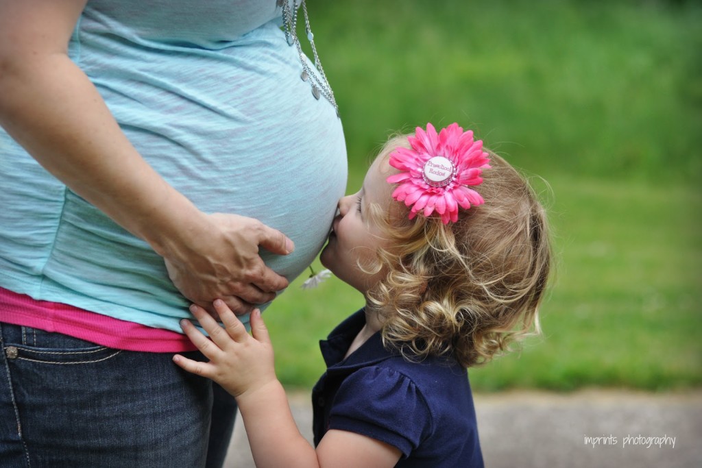 Pregnant mother and daughter kissing belly