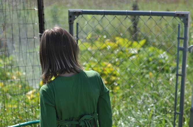 Girl walking through gate to garden by Katie M. Reid