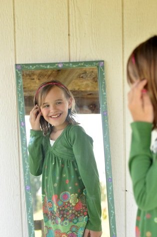 Girl looking in mirror and smiling by Katie M. Reid photography